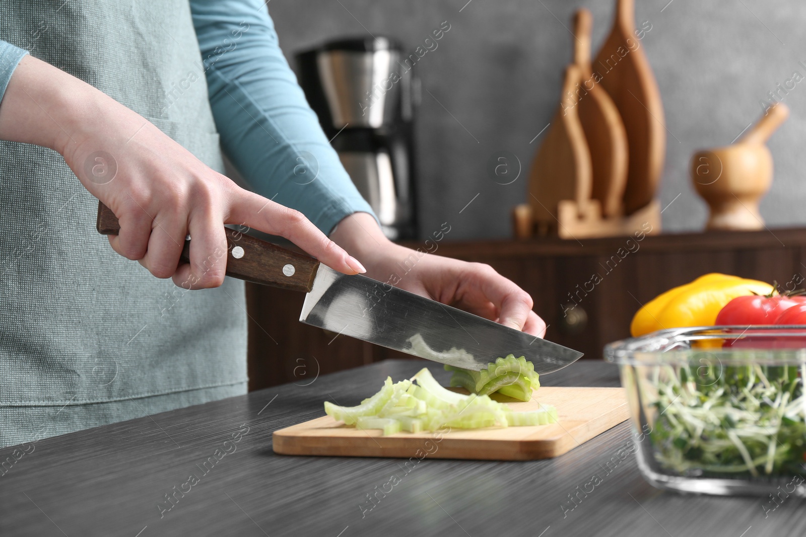 Photo of Healthy food. Woman cutting celery at black wooden table, closeup