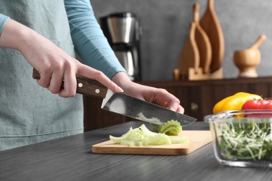 Healthy food. Woman cutting celery at black wooden table, closeup