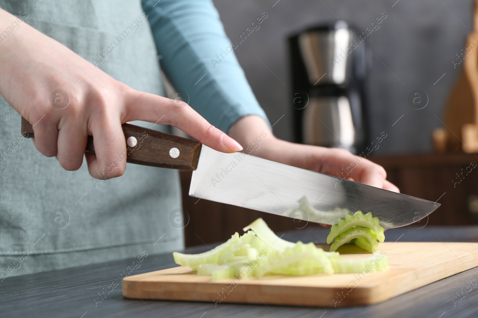 Photo of Healthy food. Woman cutting celery at black wooden table, closeup