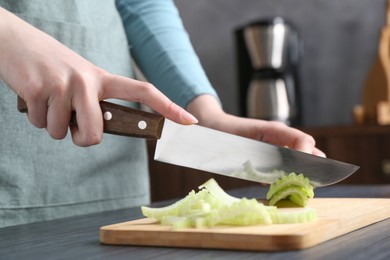 Healthy food. Woman cutting celery at black wooden table, closeup