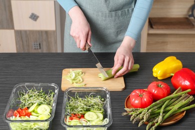 Healthy food. Woman cutting celery at black wooden table, closeup