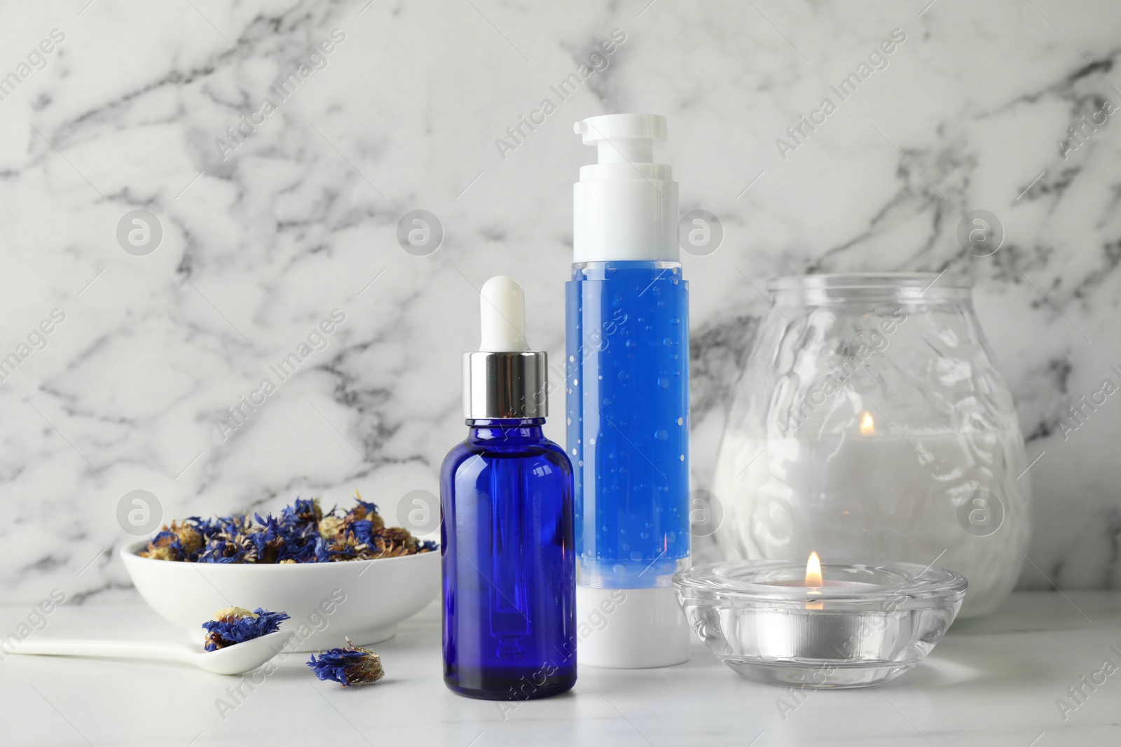 Photo of Spa composition. Bottles of cosmetic products, dry flowers and burning candles on white marble table