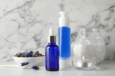 Spa composition. Bottles of cosmetic products, dry flowers and burning candles on white marble table