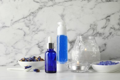 Spa composition. Bottles of cosmetic products, dry flowers and burning candles on white marble table