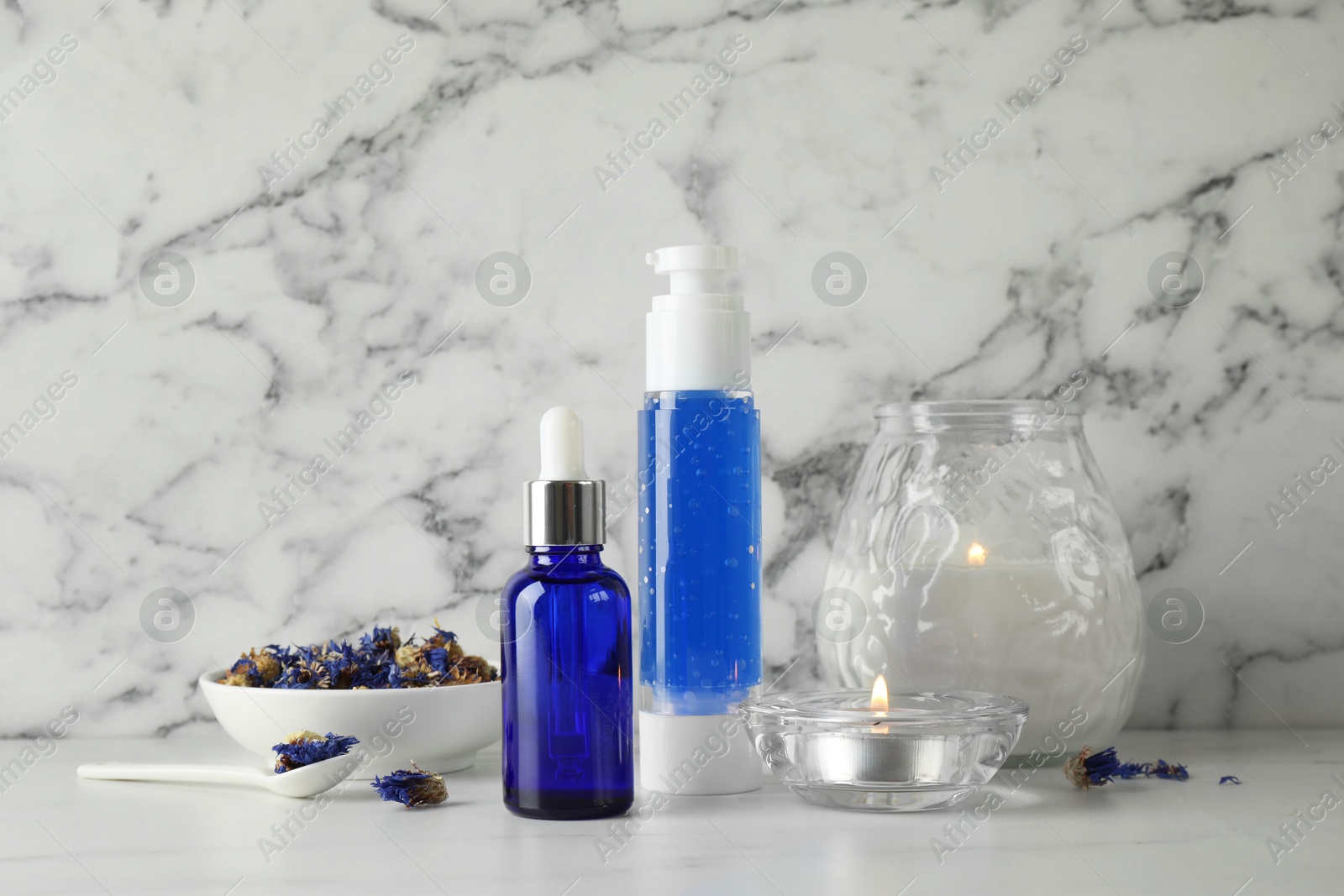 Photo of Spa composition. Bottles of cosmetic products, dry flowers and burning candles on white marble table