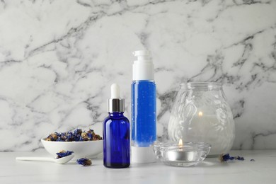 Spa composition. Bottles of cosmetic products, dry flowers and burning candles on white marble table