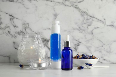 Photo of Spa composition. Bottles of cosmetic products, dry flowers and burning candles on white marble table