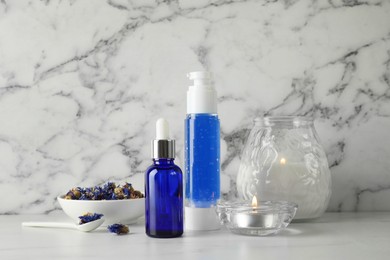 Spa composition. Bottles of cosmetic products, dry flowers and burning candles on white marble table