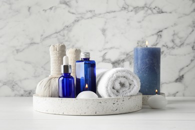 Spa composition. Bottles of cosmetic products, towel, herbal bags and burning candles on white wooden table