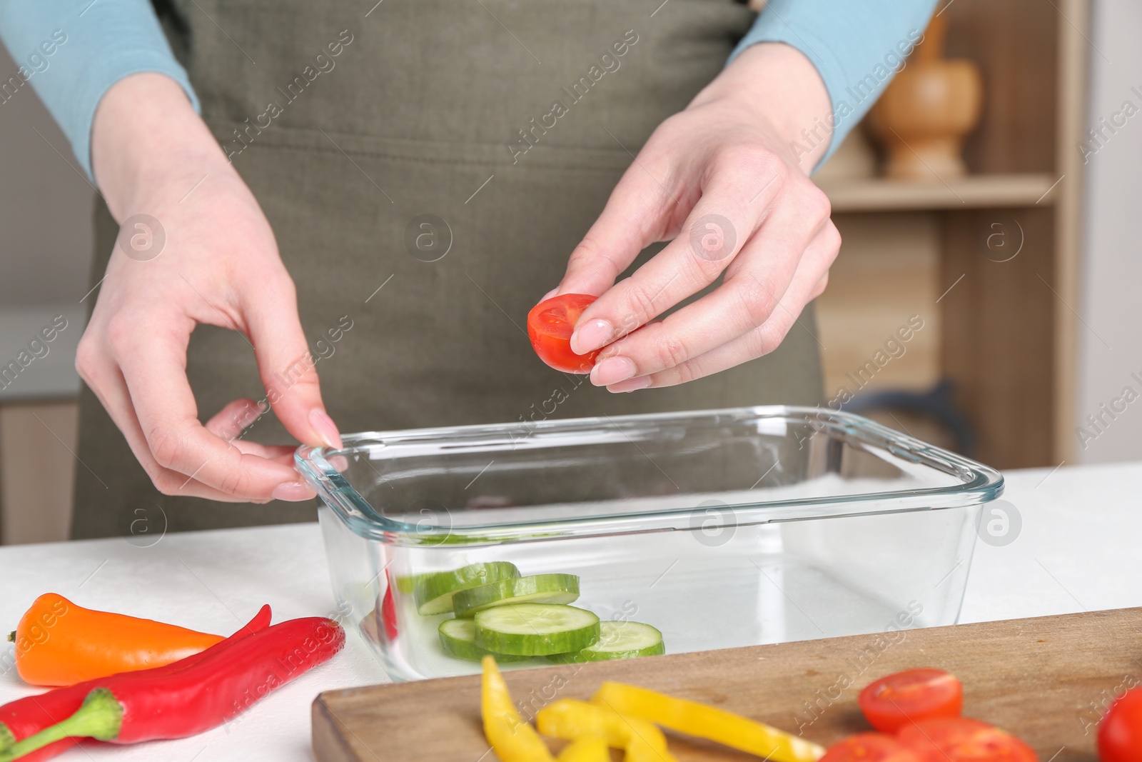 Photo of Healthy food. Woman putting piece of tomato into glass container at white table in kitchen, closeup