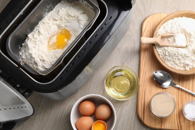 Photo of Making dough. Breadmaker and ingredients on wooden table, flat lay