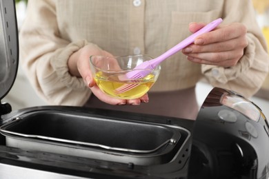 Photo of Woman spreading breadmaker pan with oil, closeup