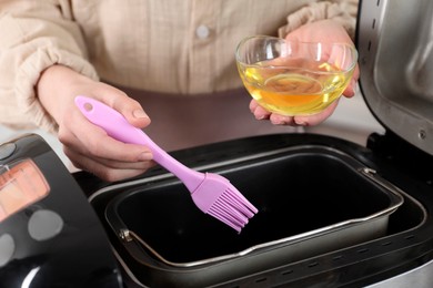 Photo of Woman spreading breadmaker pan with oil, closeup