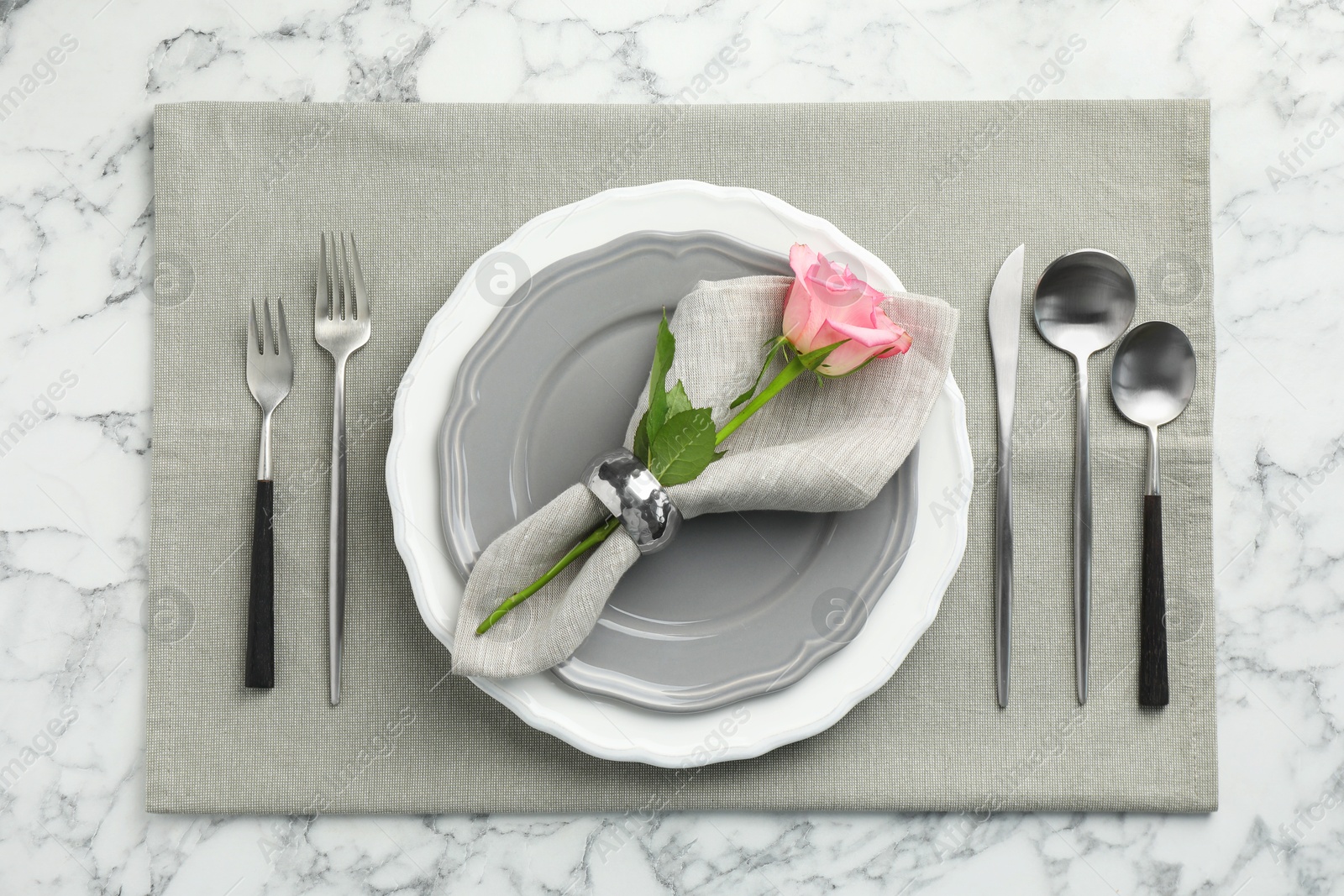 Photo of Stylish setting with cutlery, rose and plates on white marble table, flat lay