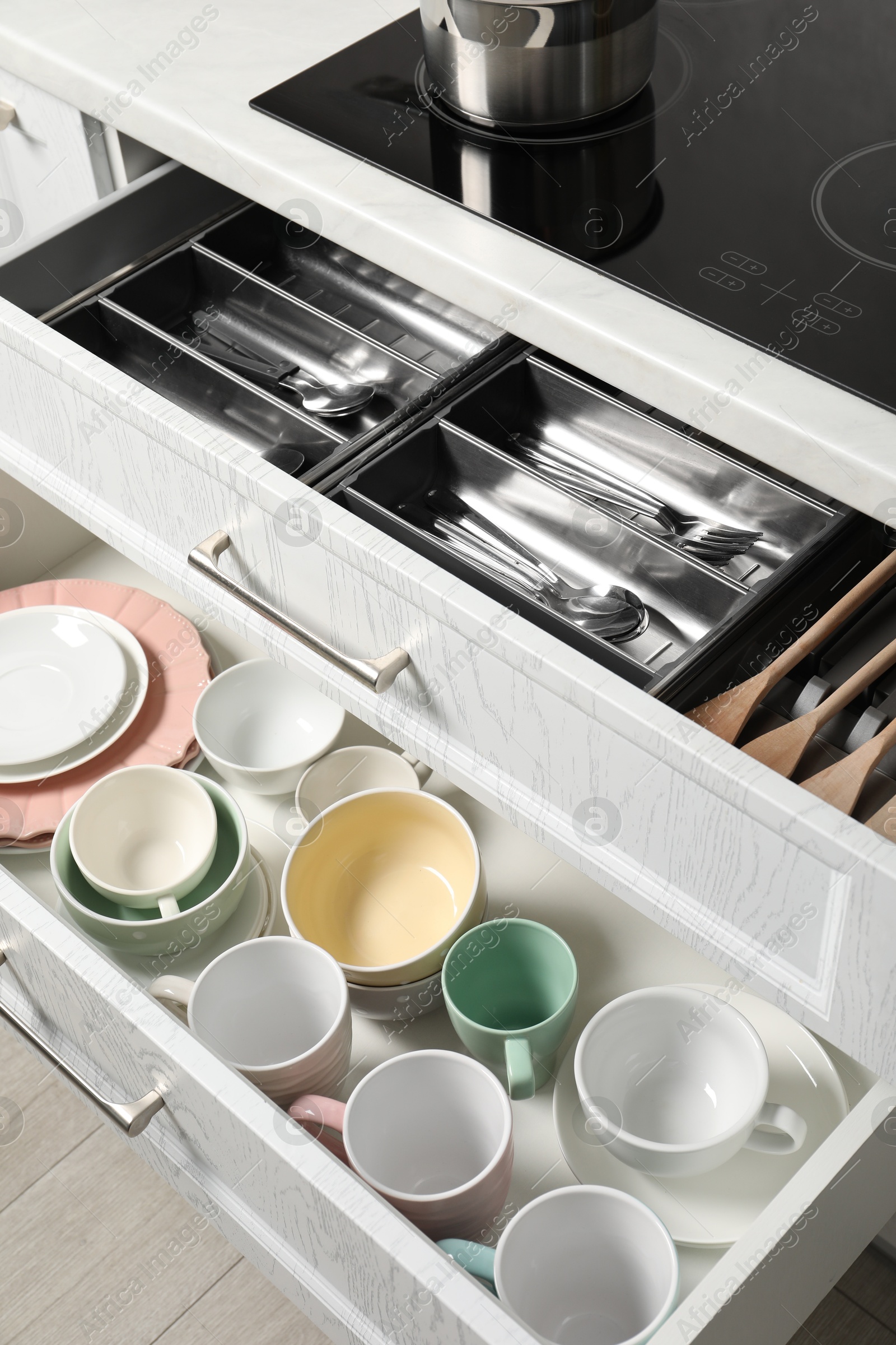 Photo of Ceramic dishware, utensils and cutlery in drawers indoors