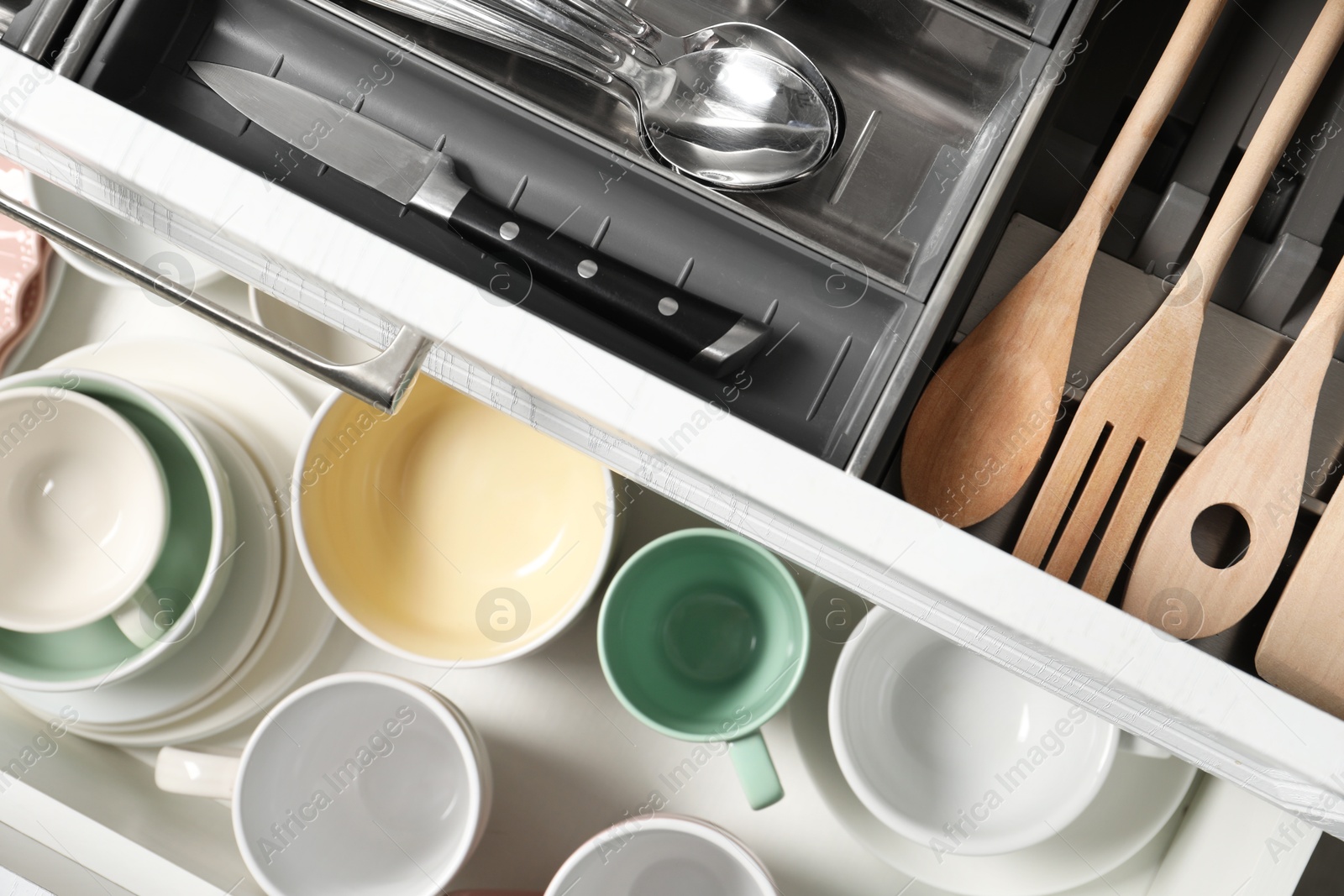 Photo of Ceramic dishware, utensils and cutlery in drawers, top view