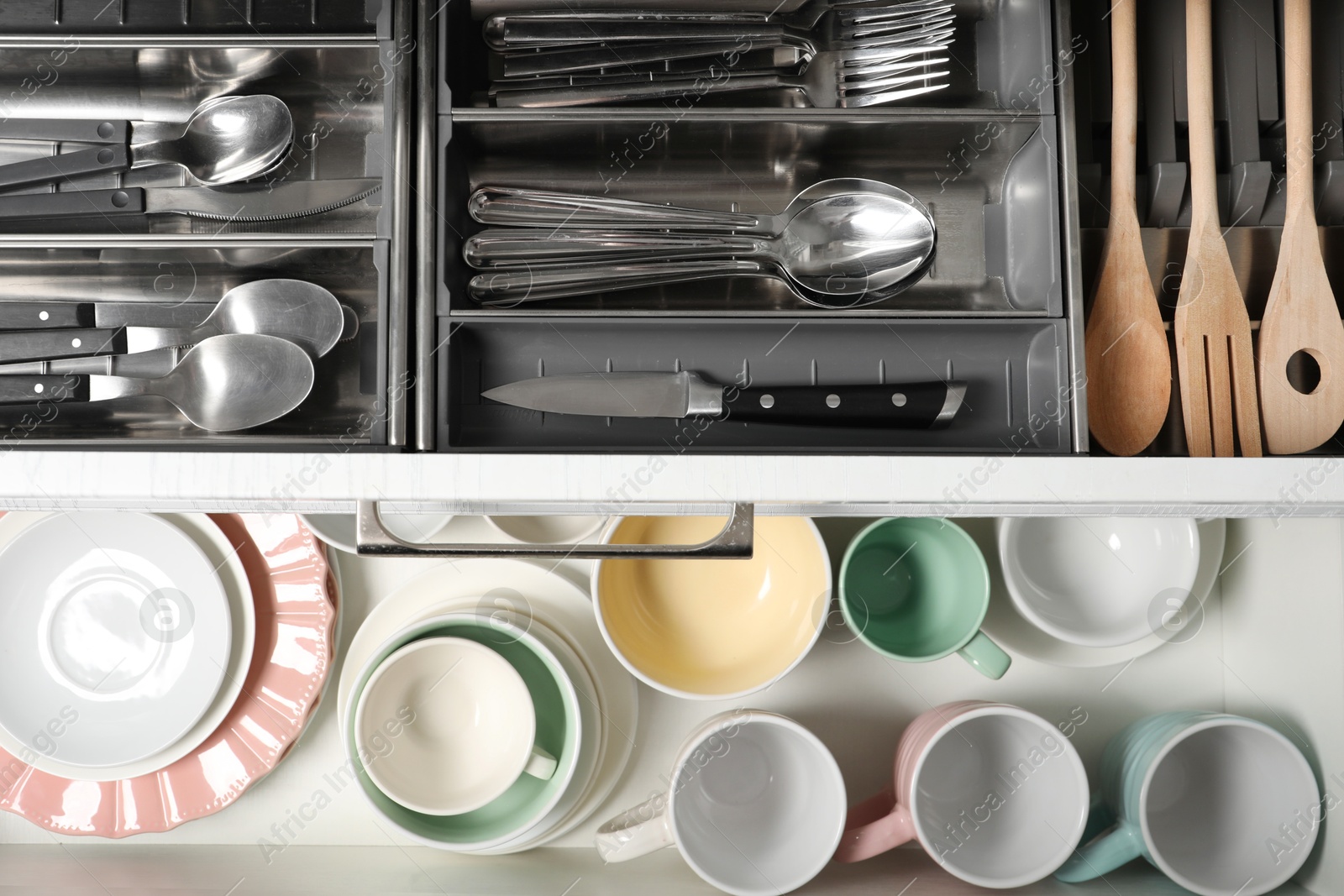 Photo of Ceramic dishware, utensils and cutlery in drawers, top view