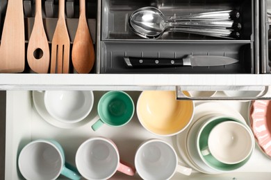 Photo of Ceramic dishware, utensils and cutlery in drawers, top view