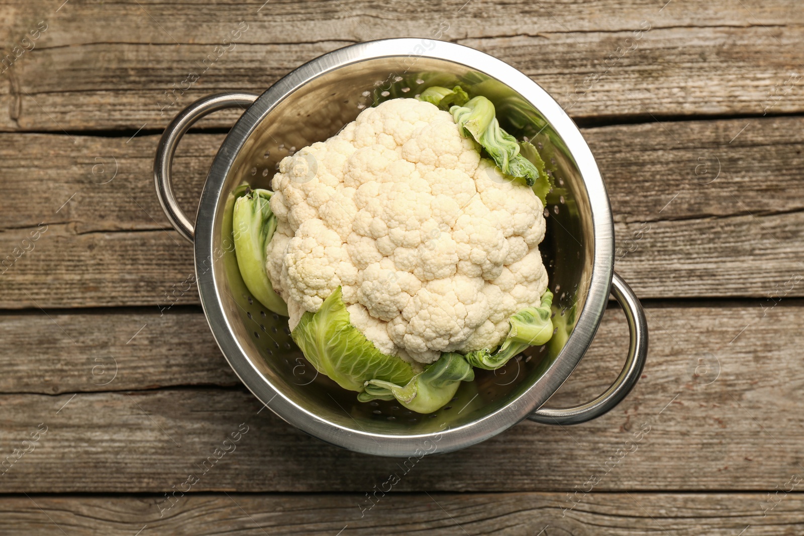 Photo of Metal colander with cauliflower on wooden table, top view