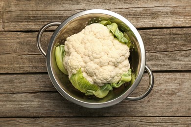 Metal colander with cauliflower on wooden table, top view