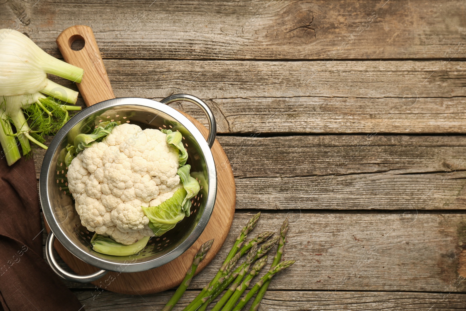 Photo of Metal colander with cauliflower, fennel and asparagus on wooden table, flat lay. Space for text