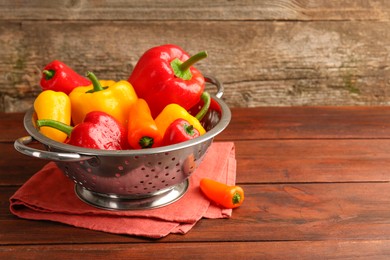Photo of Metal colander with fresh peppers on wooden table, space for text