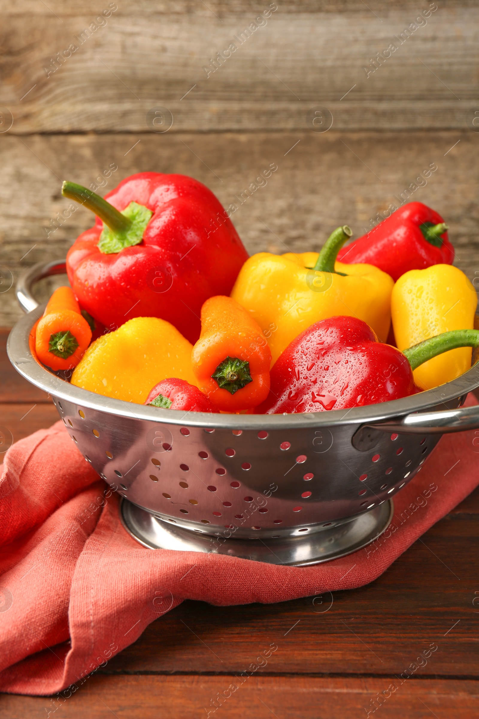 Photo of Metal colander with fresh peppers on wooden table, closeup