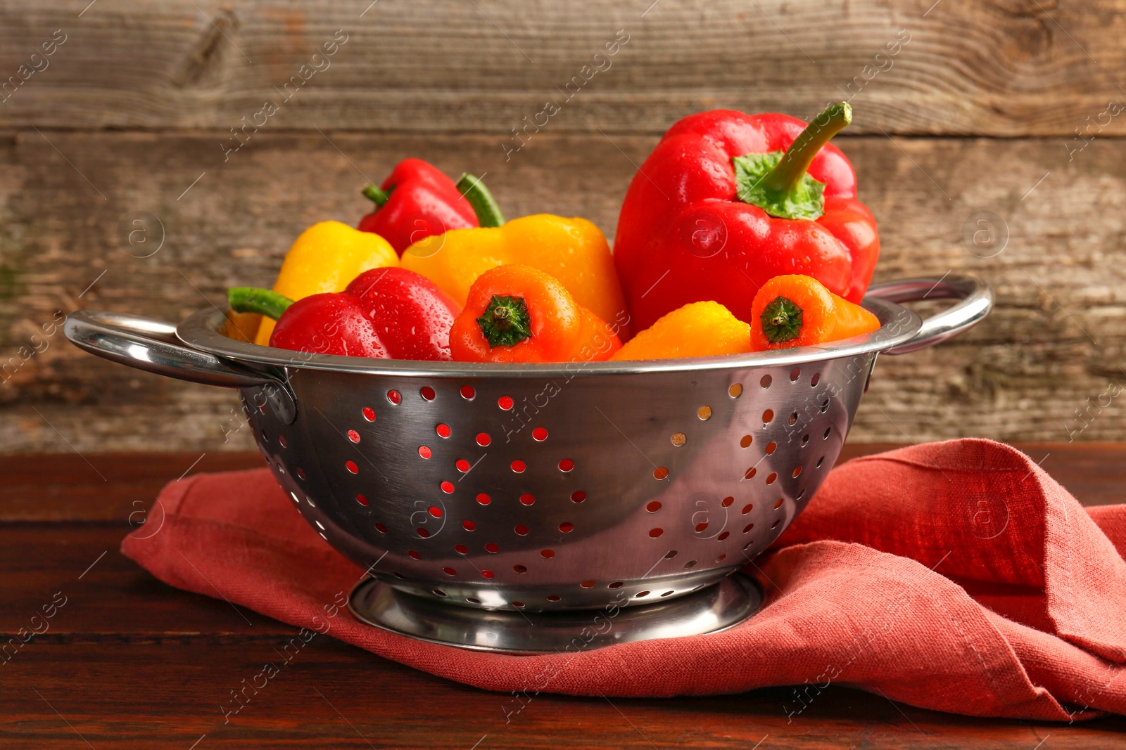 Photo of Metal colander with fresh peppers on wooden table, closeup