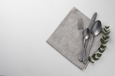 Stylish setting with cutlery and napkin on white textured table, top view. Space for text
