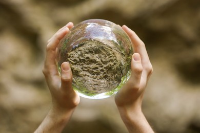 Photo of Stone surface outdoors, overturned reflection. Man holding crystal ball in forest, closeup