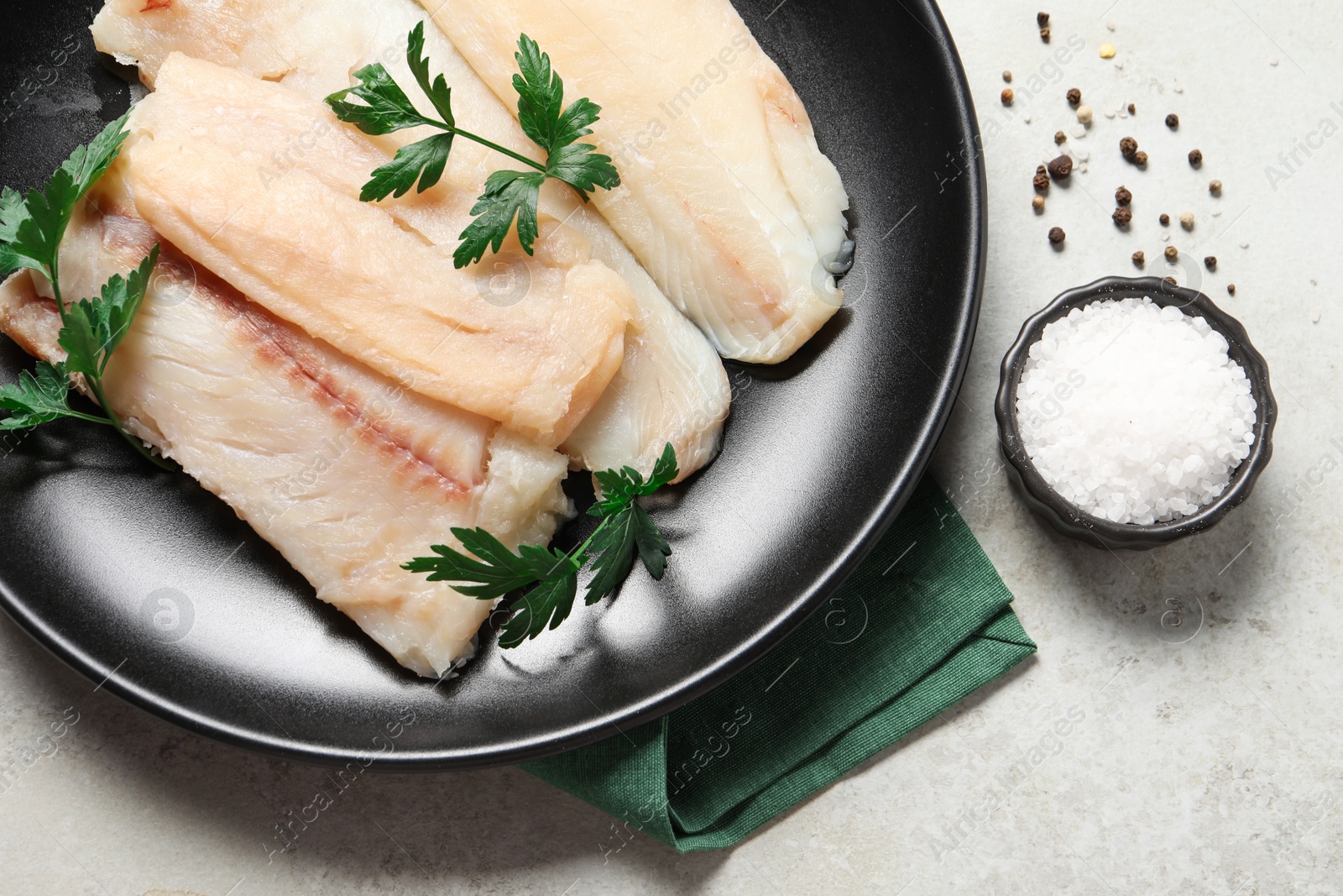 Photo of Plate with raw cod fish, spices and parsley on light table, flat lay