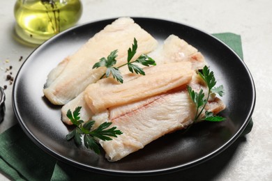 Photo of Plate with raw cod fish and parsley on light table, closeup