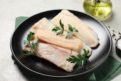 Photo of Plate with raw cod fish and parsley on light table, closeup