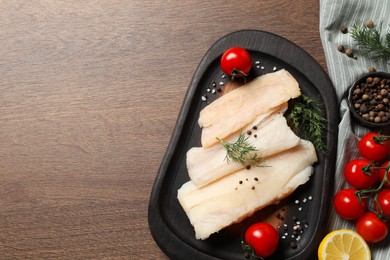 Raw cod fish, dill, lemon, tomatoes and spices on wooden table, top view. Space for text