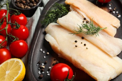 Photo of Raw cod fish, dill, lemon, tomatoes and spices on table, closeup