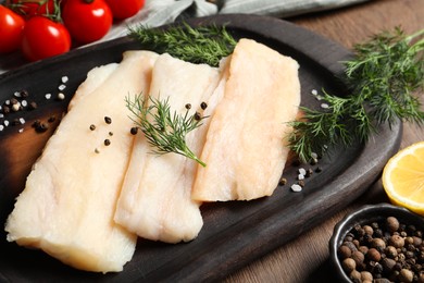 Photo of Raw cod fish, dill and spices on wooden table, closeup