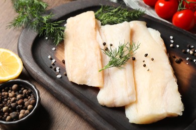 Photo of Raw cod fish, dill and spices on wooden table, closeup
