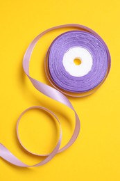Photo of Beautiful violet ribbon reel on yellow background, top view