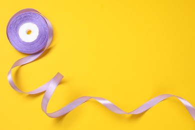Photo of Beautiful violet ribbon reel on yellow background, top view. Space for text