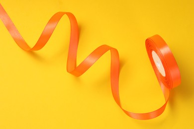 Photo of Beautiful orange ribbon reel on yellow background, top view