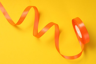 Beautiful orange ribbon reel on yellow background, top view