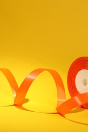 Photo of Beautiful orange ribbon reel on yellow background, closeup