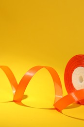 Beautiful orange ribbon reel on yellow background, closeup