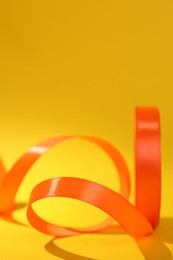 Photo of Beautiful orange ribbon reel on yellow background, closeup