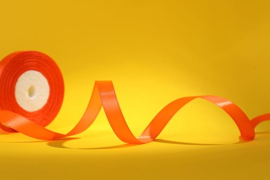Photo of Beautiful orange ribbon reel on yellow background, closeup