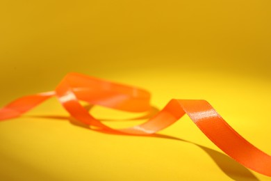 Photo of Beautiful orange ribbon on yellow background, closeup