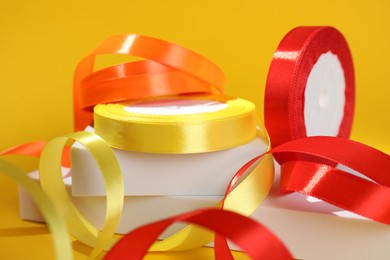 Photo of Beautiful ribbon reels and different podiums on yellow background, closeup