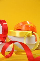 Photo of Beautiful ribbon reels and different podiums on yellow background, closeup