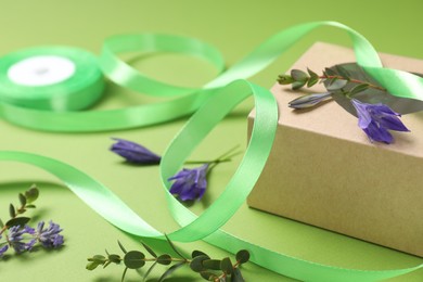 Photo of Beautiful ribbon with flowers and gift box on green background, closeup