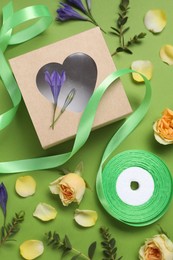 Flat lay composition with beautiful ribbon reel and gift box on green background